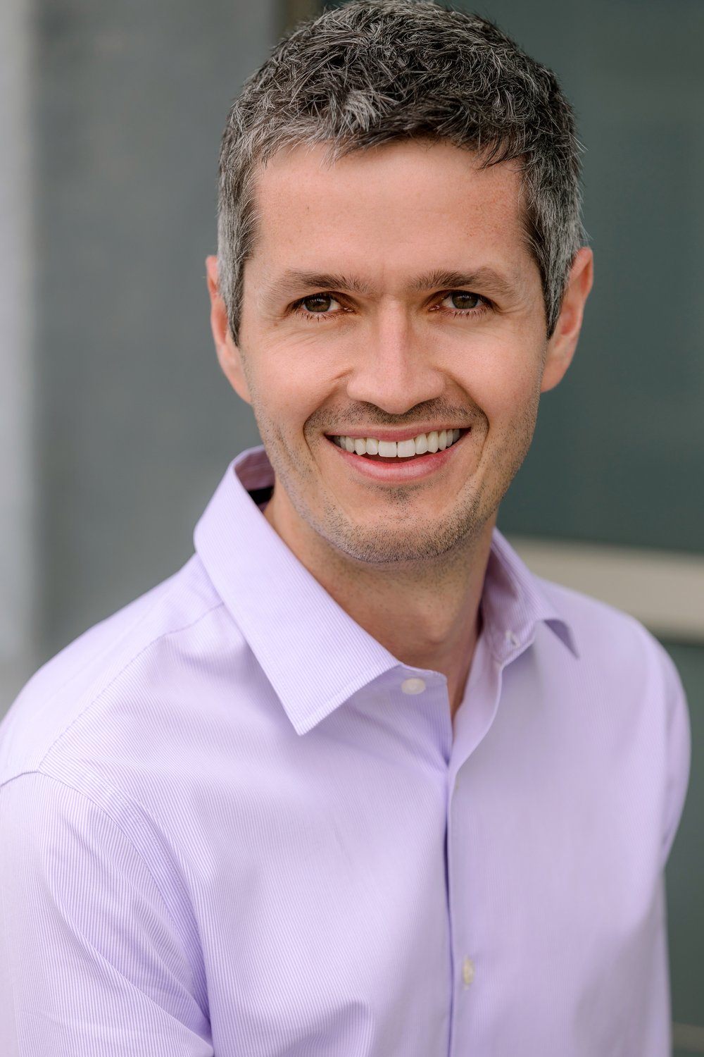 Man with short salt-n-pepper hair, smiling, and wearing a lavendar shirt