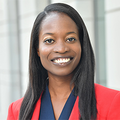 Woman with long straight hair and a smile, wearing a red suit jacket