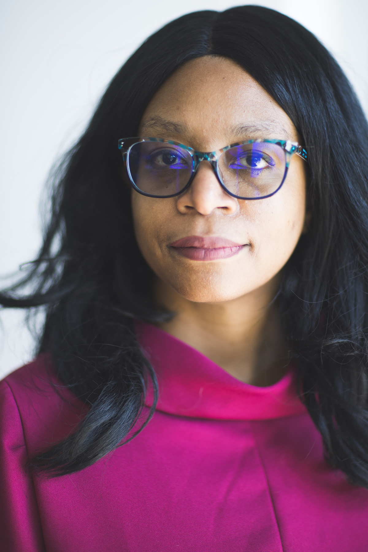 African-American woman with long, dark hair, glasses, wearing a bright fuschia shirt.