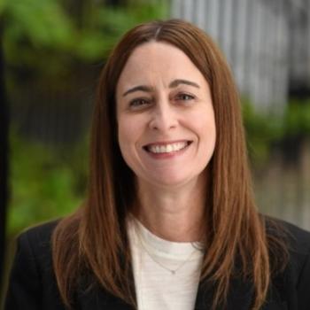 Woman smiling with medium length brown hair against an outdoor backdrop