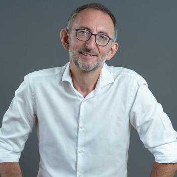 Man sitting with a white collared shirt, glasses, and salt and pepper hair
