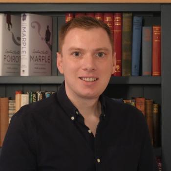 Man with ginger colored hair smiling in front of a bookcase