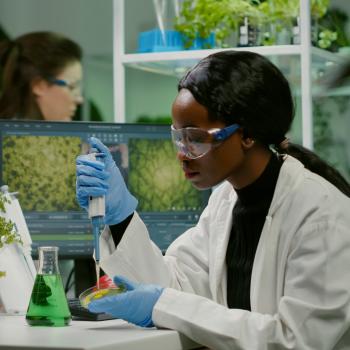 African American woman working in a science lab, wearing blue latex gloves and a white coat.